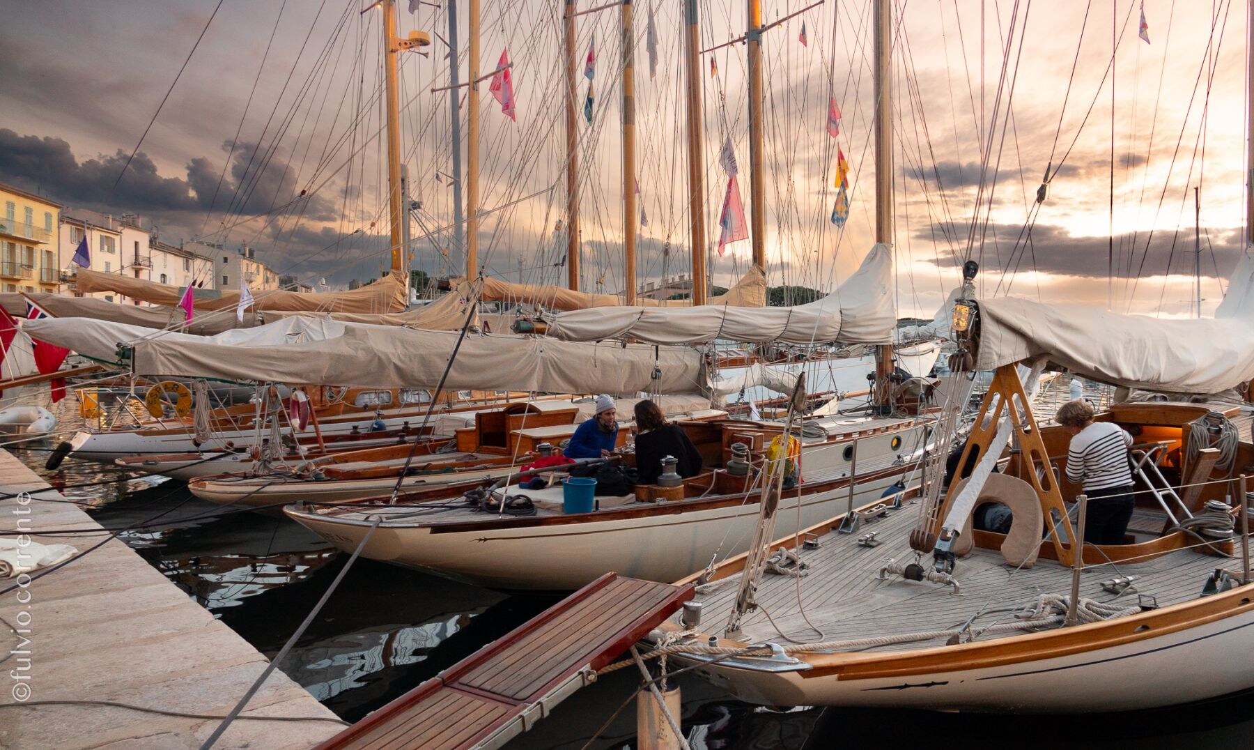 Voiliers classiques amarrés à quai au crépuscule, ciel orageux orangé.
