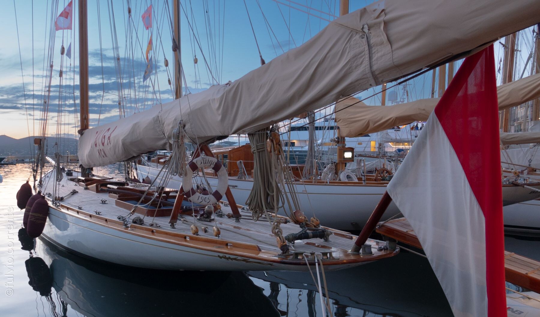 Voilier classique amarré, voile ferlée et pavillon rouge et blanc.