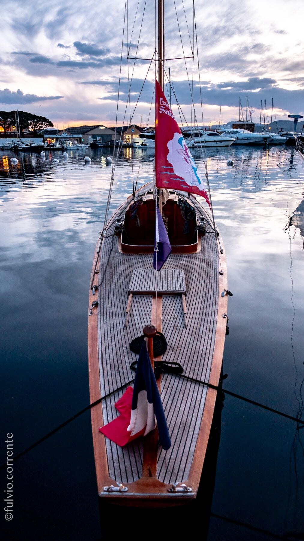 Pont en bois d’un voilier vu du dessus, au port, reflets dans l’eau.