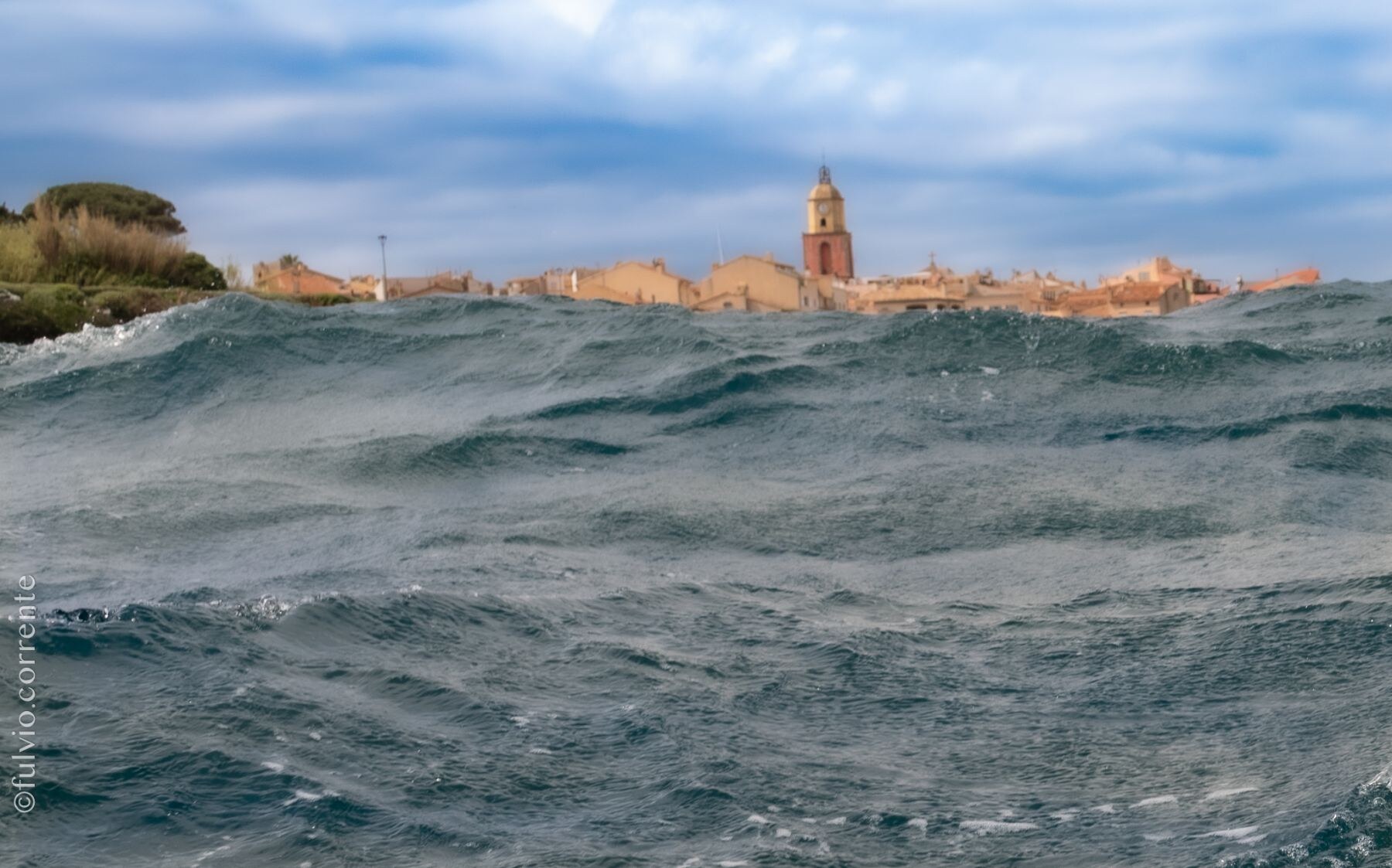 Mer agitée au premier plan, village de Saint-Tropez à l’horizon.