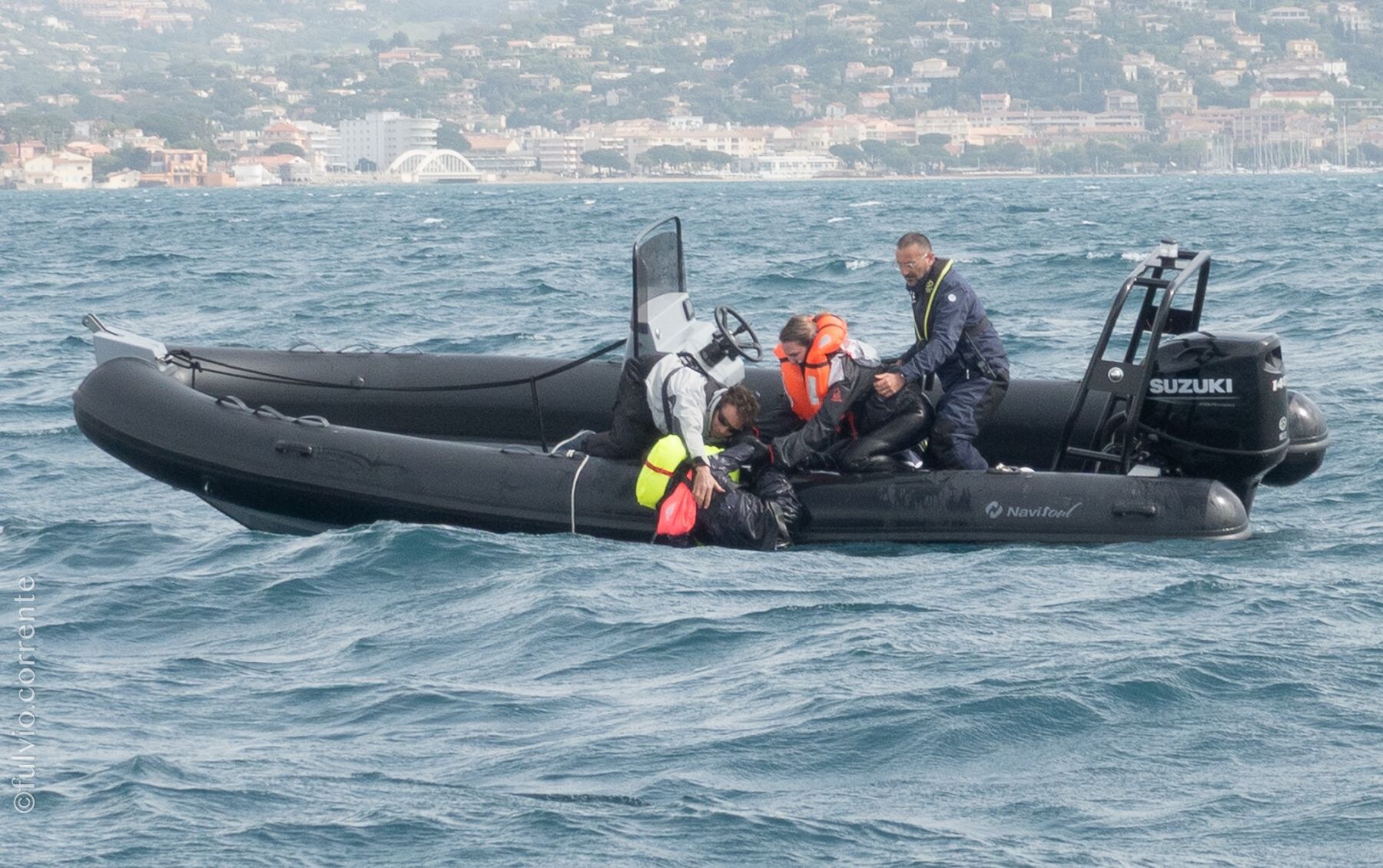 Deux semi-rigides noirs sur une mer agitée, ville côtière au loin.