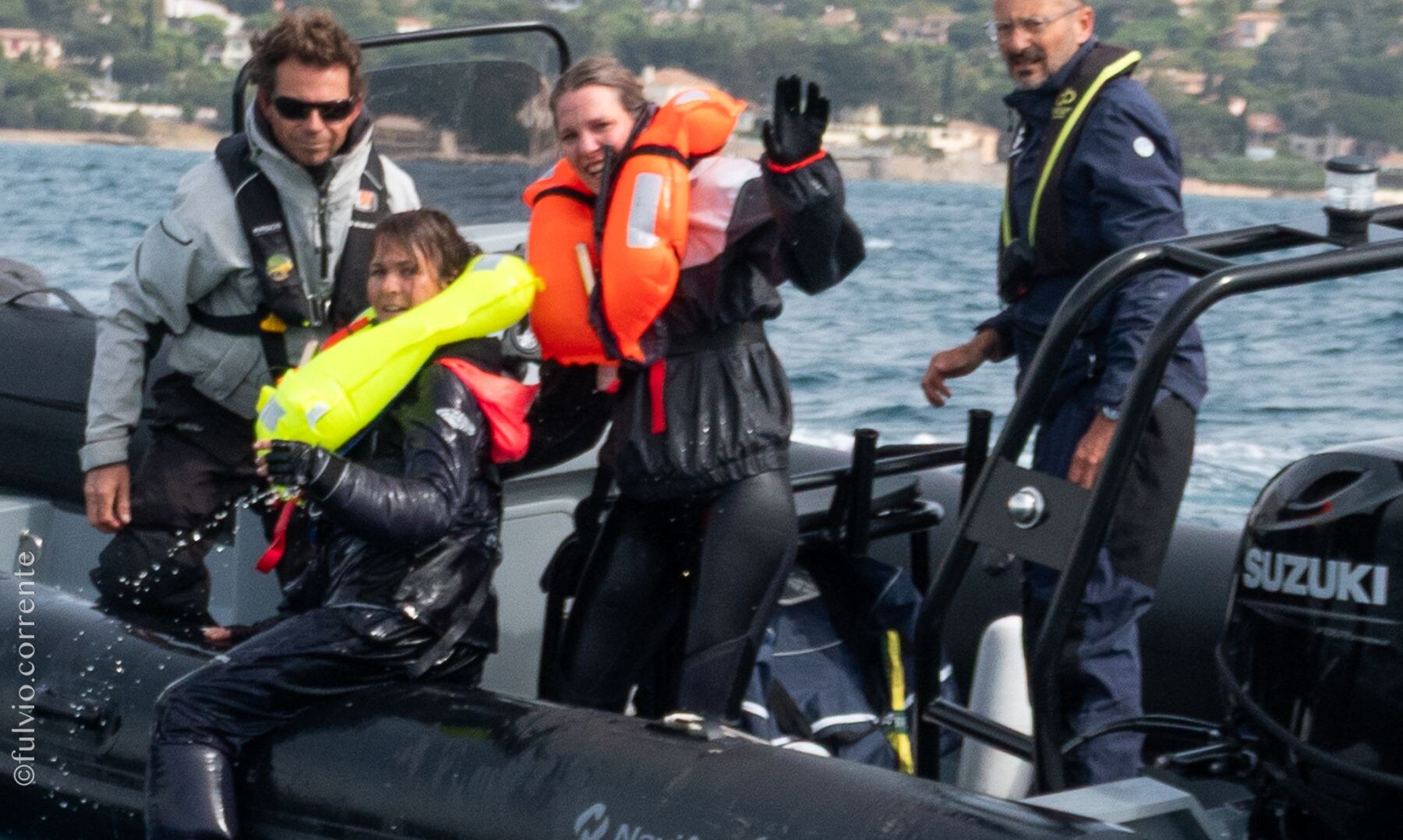 Équipières en gilets de sauvetage à bord d’un semi-rigide, l’une salue.