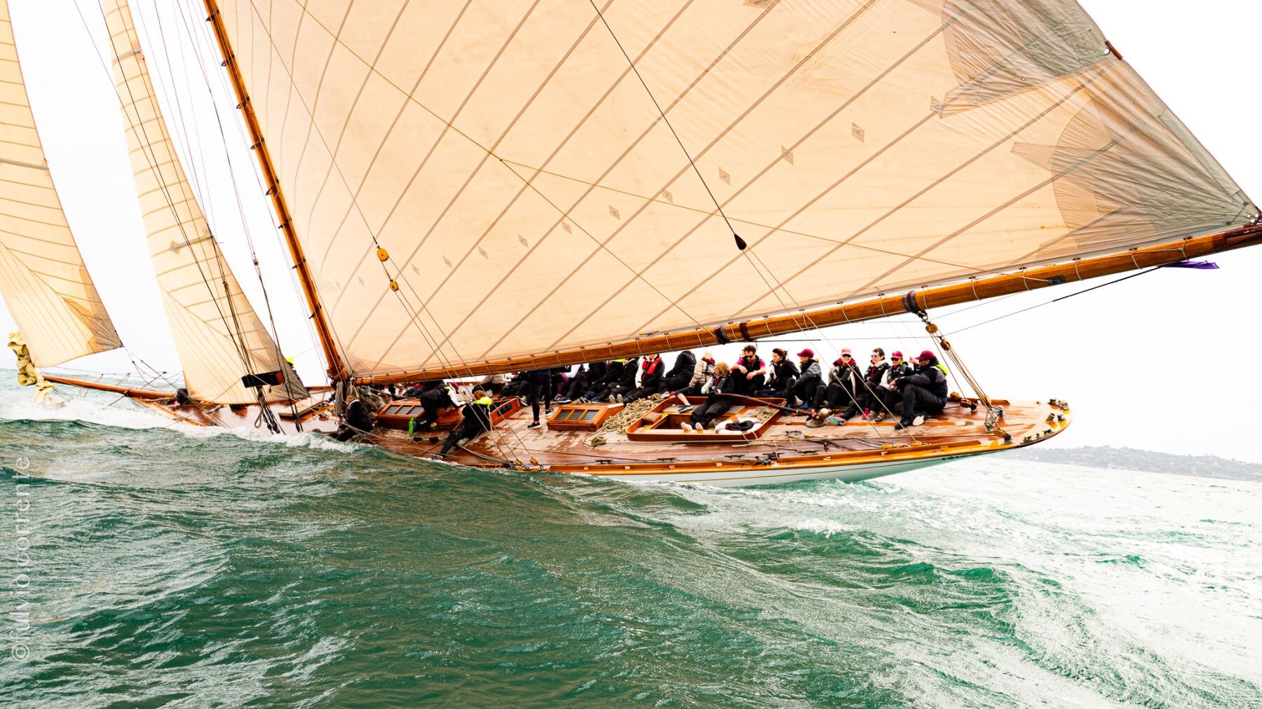 Voilier à grande voile ocre et équipage serré sur le pont, mer verte.