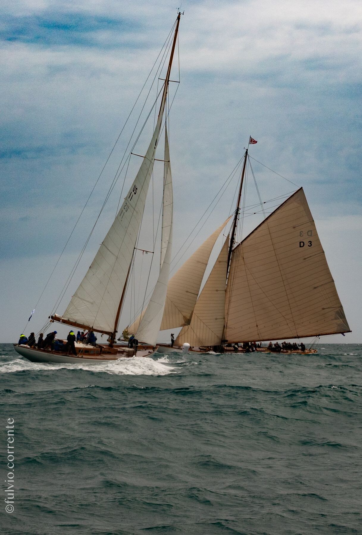 Deux voiliers classiques à voiles beiges, mer grise et ciel nuageux.