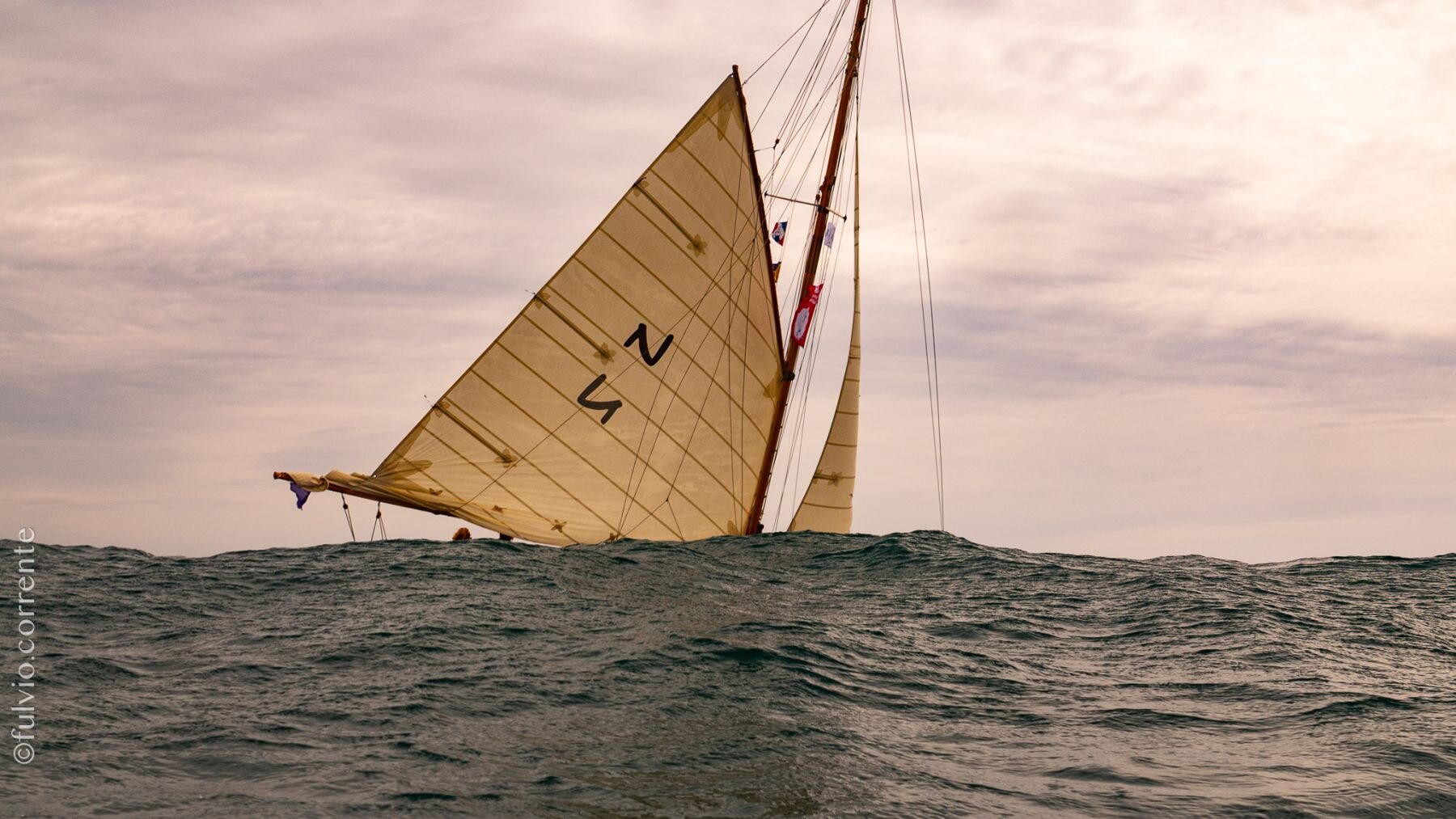 Voile beige numérotée apparaissant derrière une vague, ciel rosé.