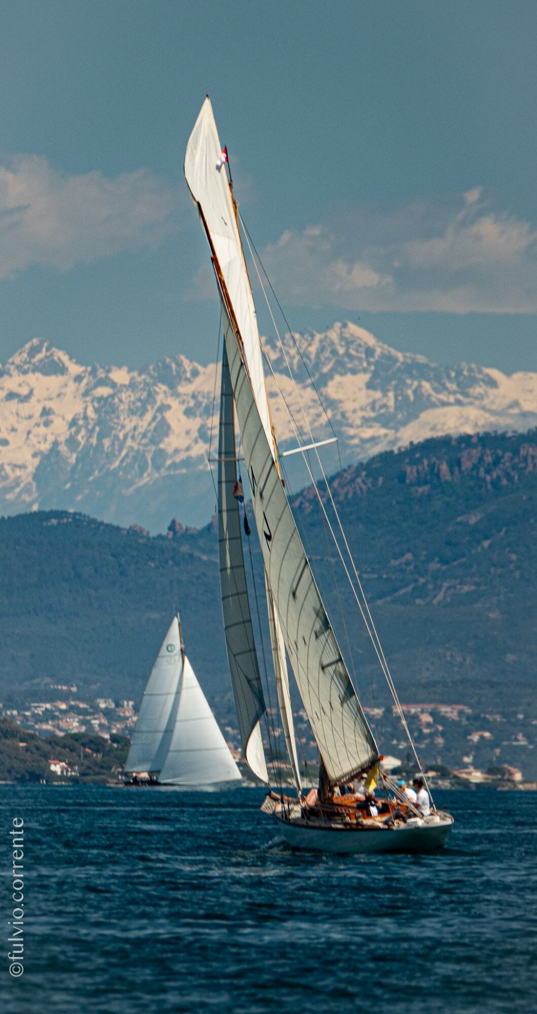 Voilier classique à haute voile devant des montagnes enneigées, un second voilier en arrière-plan.