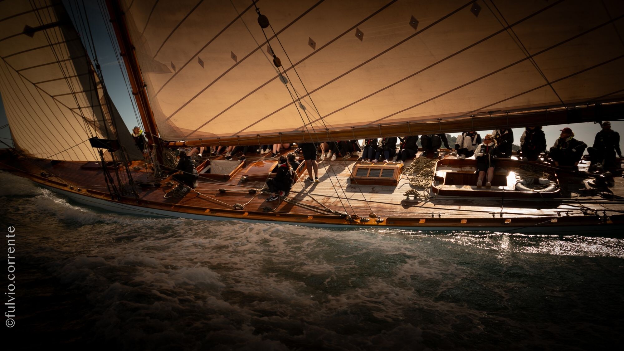 Équipage sous la grande voile d’un voilier classique, ambiance sombre et chaude.