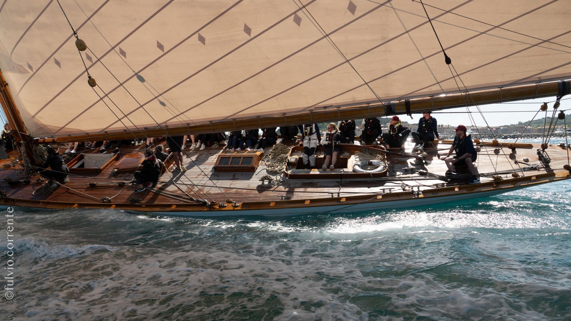 Équipage sous la grande voile beige d’un voilier classique, lumière douce.