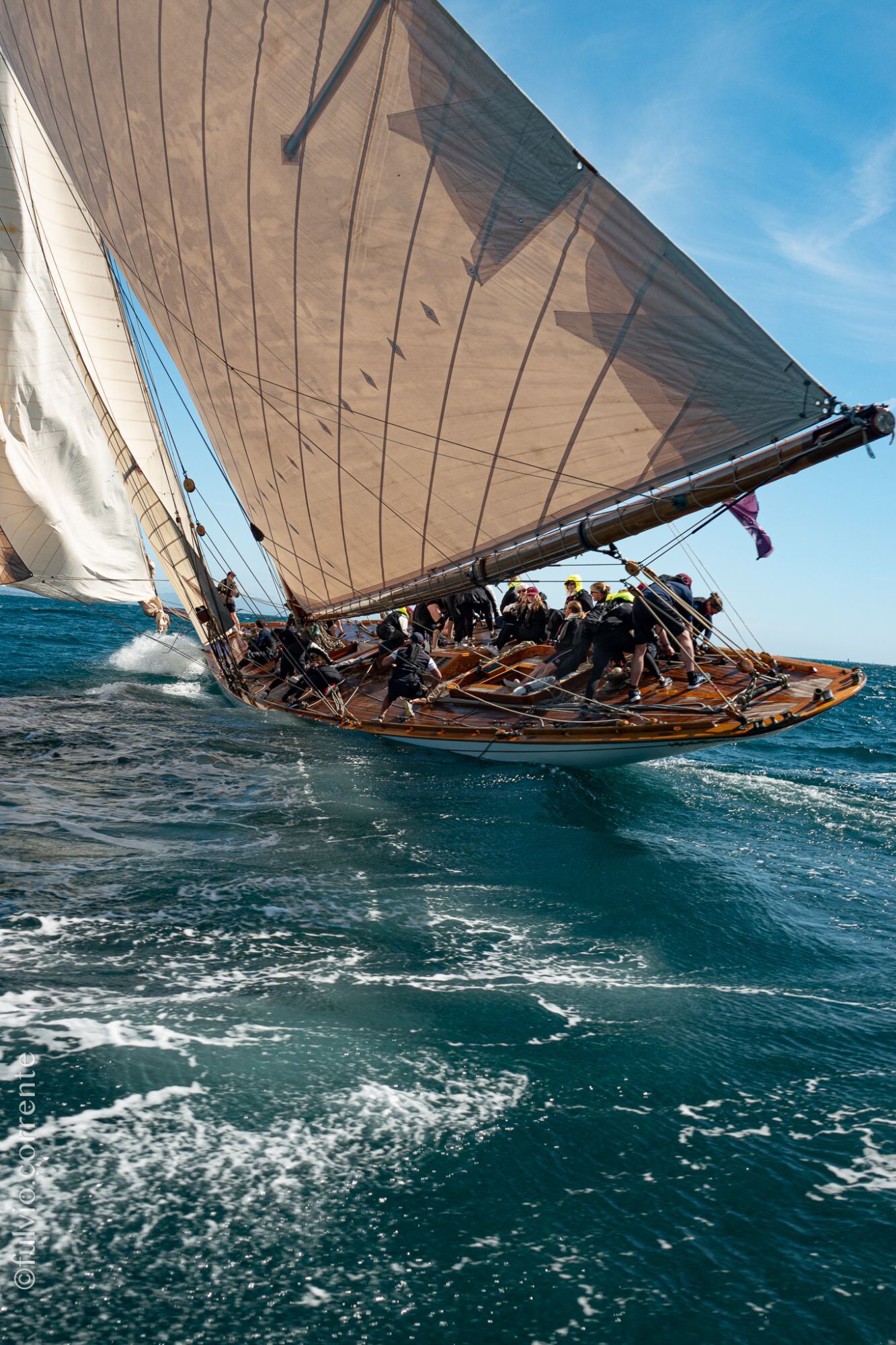 Voilier à voile brune fortement gîté, équipage en rang sur le pont.
