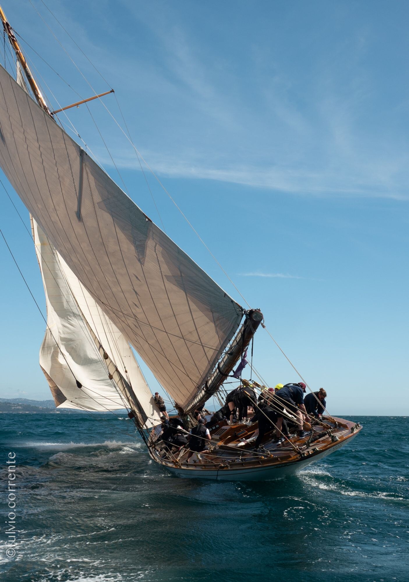 Voilier classique gîté, grande voile brune et foc, mer bleue.