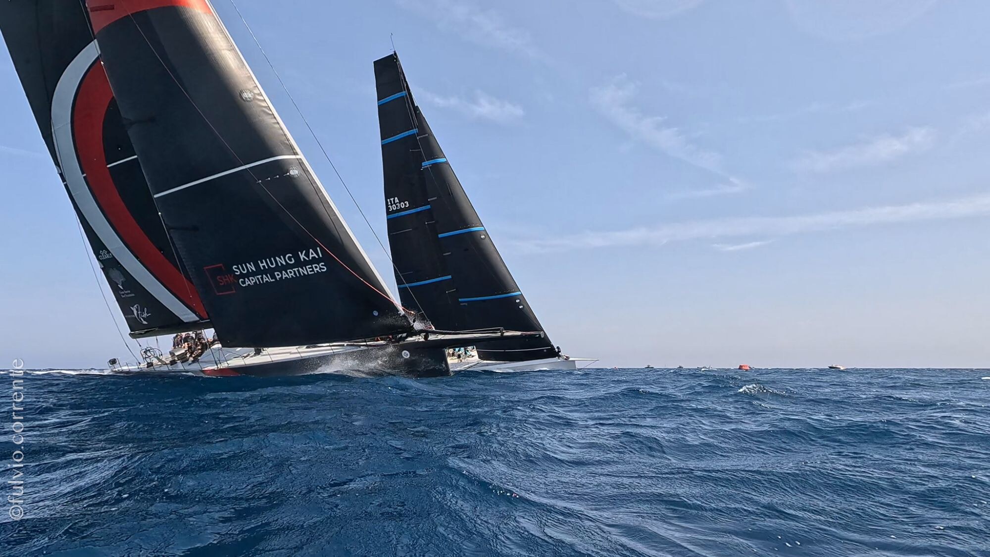 Voiliers de course aux voiles noires et rouges sur mer calme, ciel bleu.