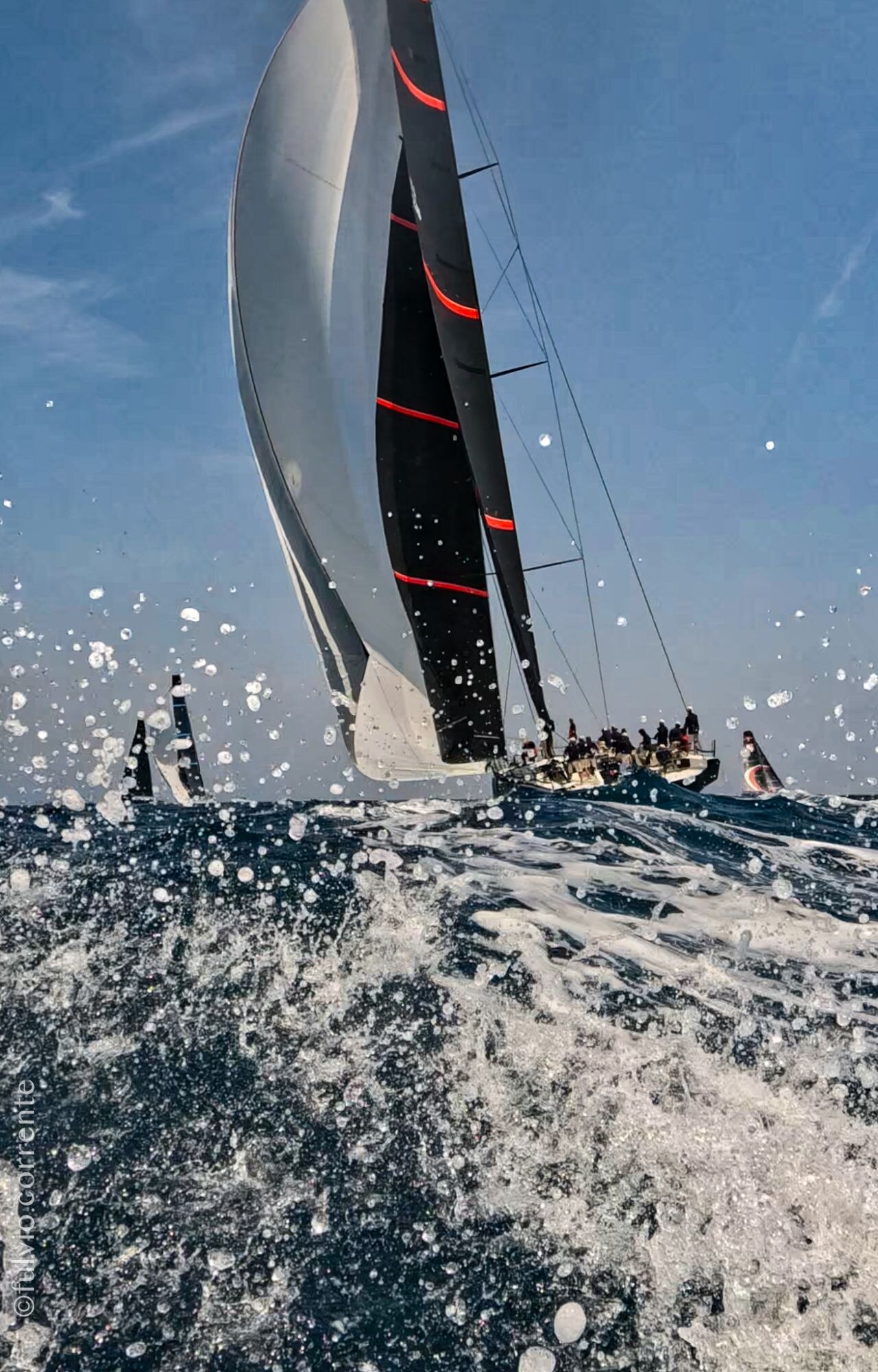 Voilier de course gîté dans les embruns, voile blanche et noire.