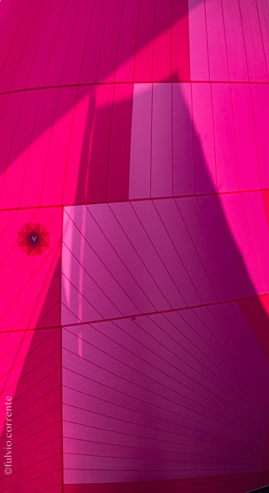 Détail d’une voile rose vif, coutures et ombres.