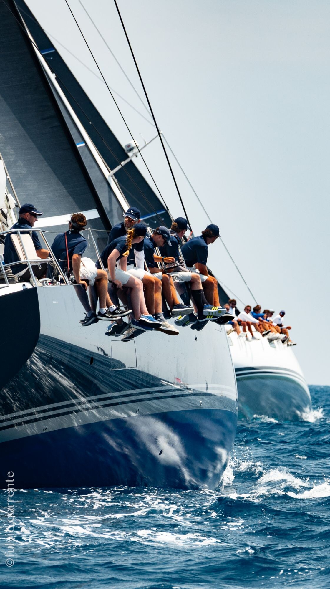 Équipage assis au rappel sur la coque bleu marine d’un grand voilier de course.