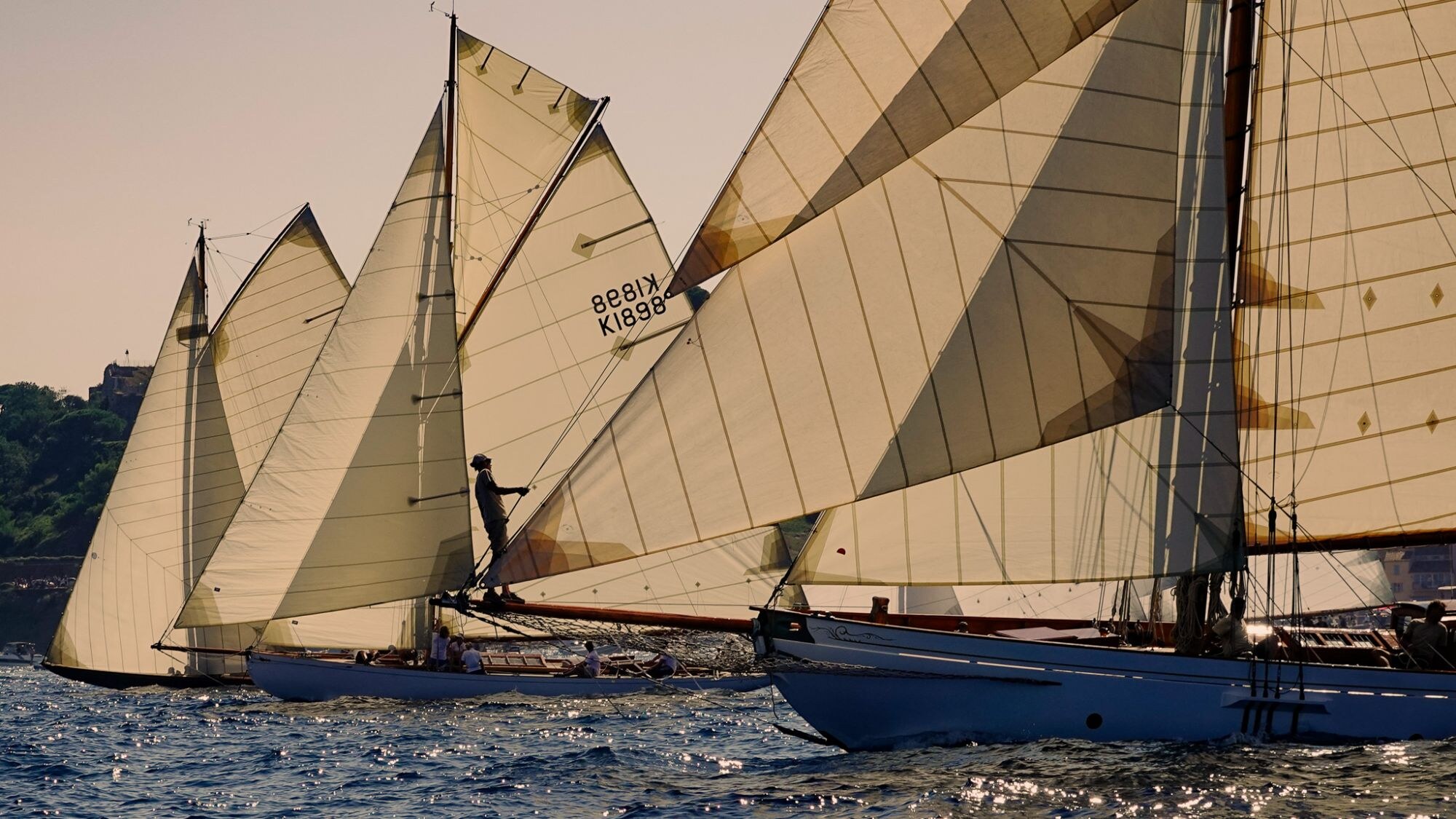 Voiliers classiques serrés en régate, voiles ocre dans une lumière chaude.