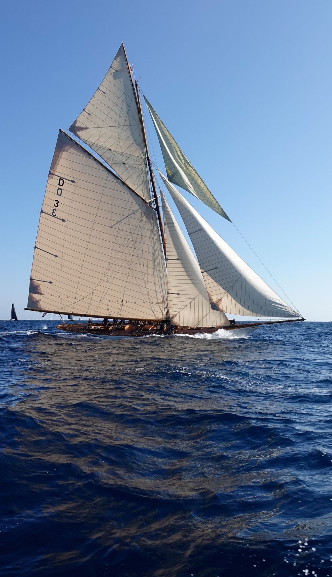 Voilier classique à voiles blanches sur une mer bleu profond.