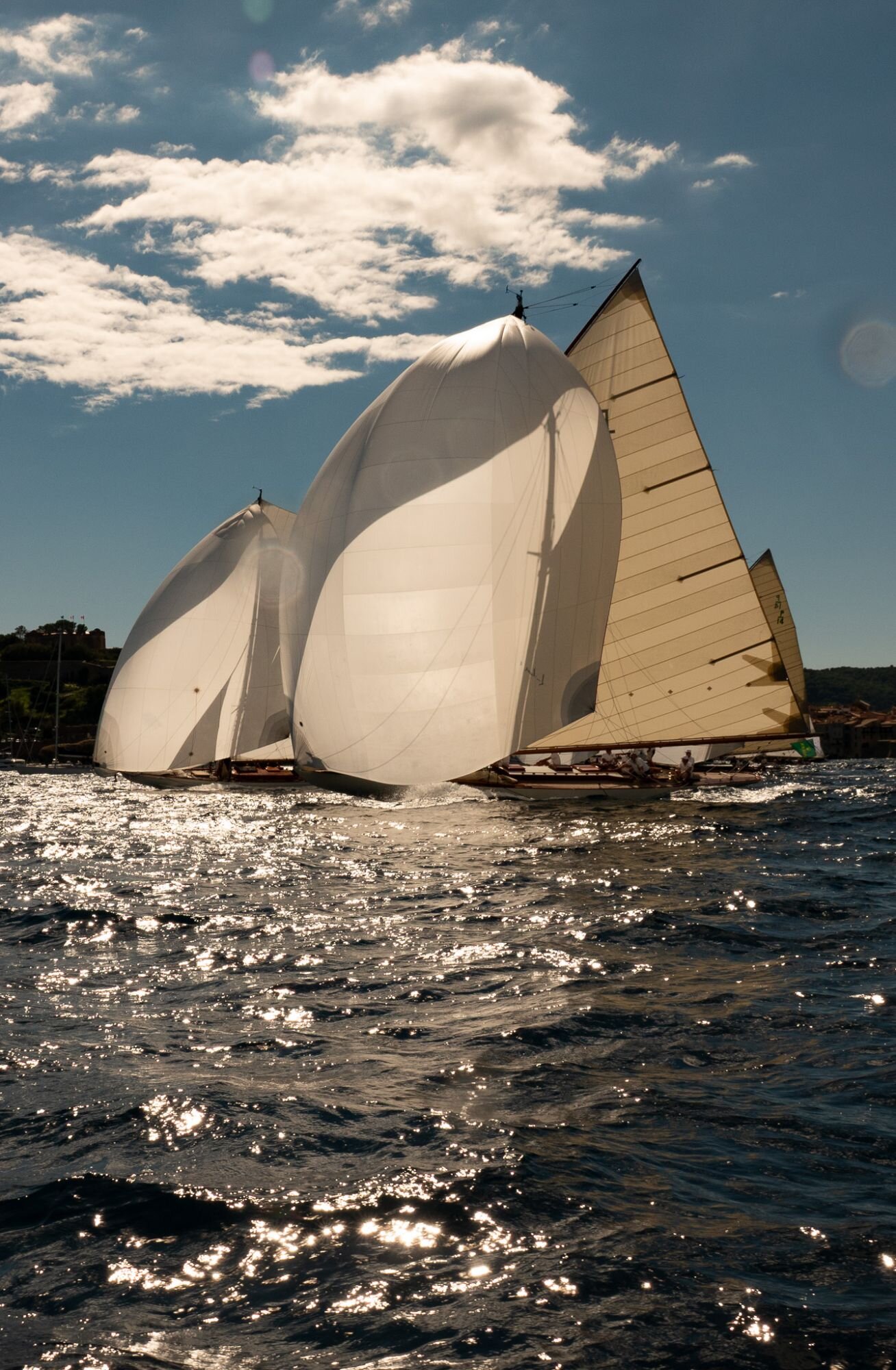 Voilier aux grandes voiles blanches gonflées sur une mer scintillante en contre-jour.