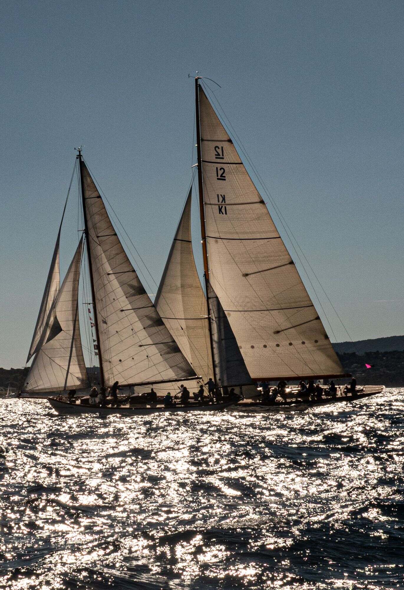 Voiliers aux voiles claires en contre-jour sur une mer scintillante.