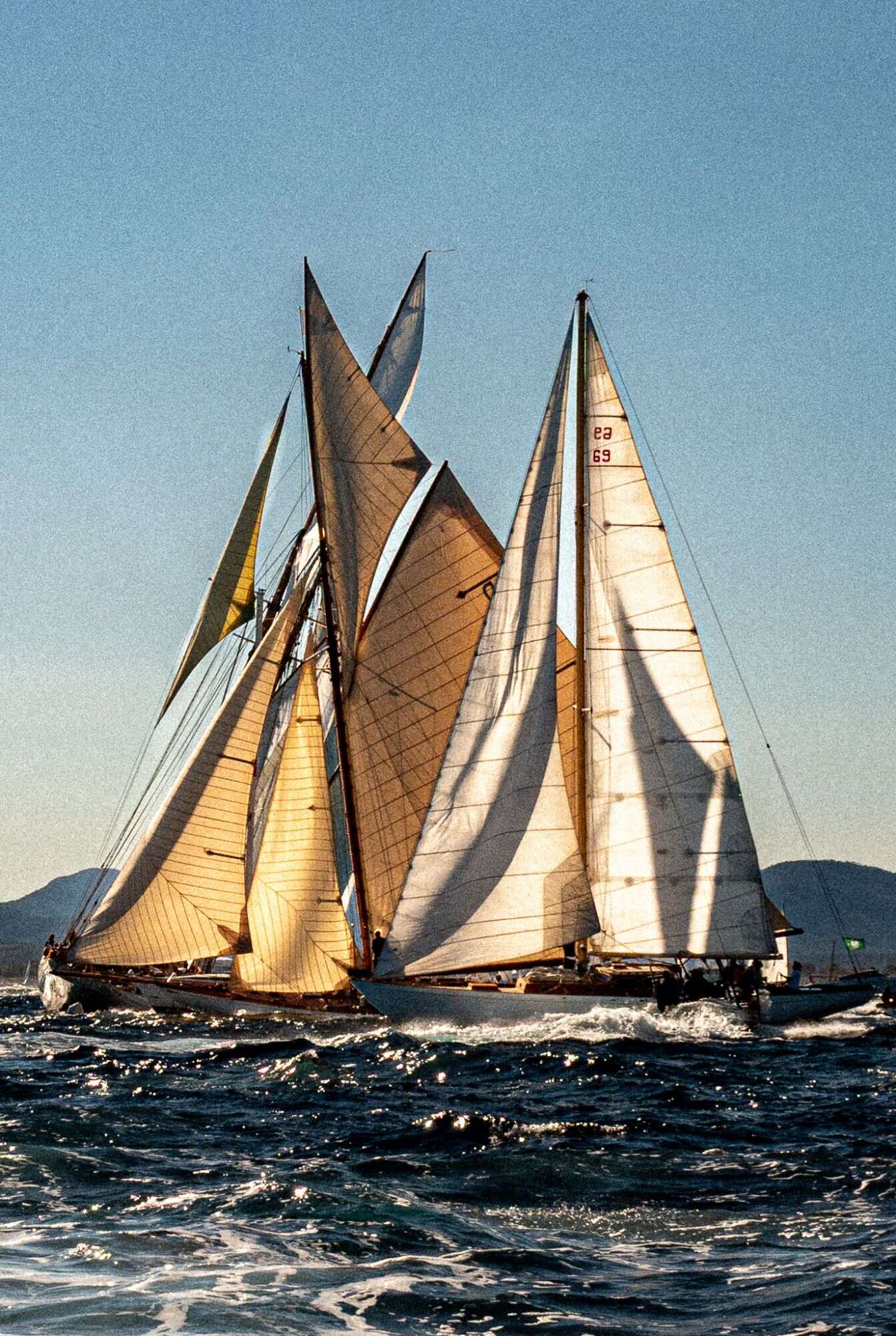 Deux voiliers classiques aux voiles croisées, mer sombre et ciel bleu-gris.