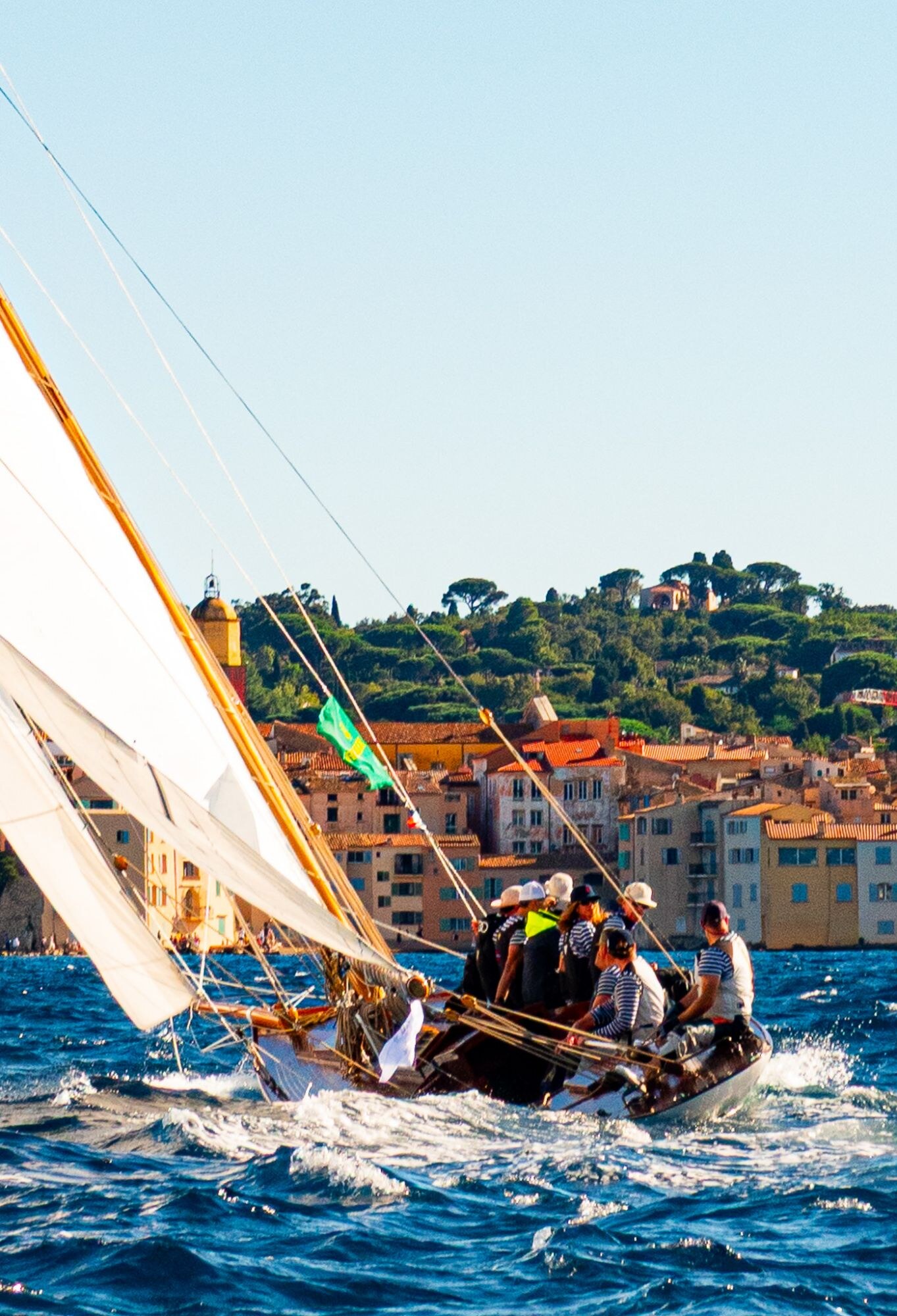 Voilier classique gîté devant les façades colorées de Saint-Tropez.