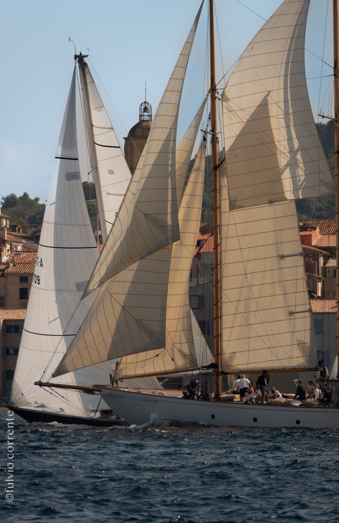 Goélette aux voiles ocre en route devant les maisons de Saint-Tropez.
