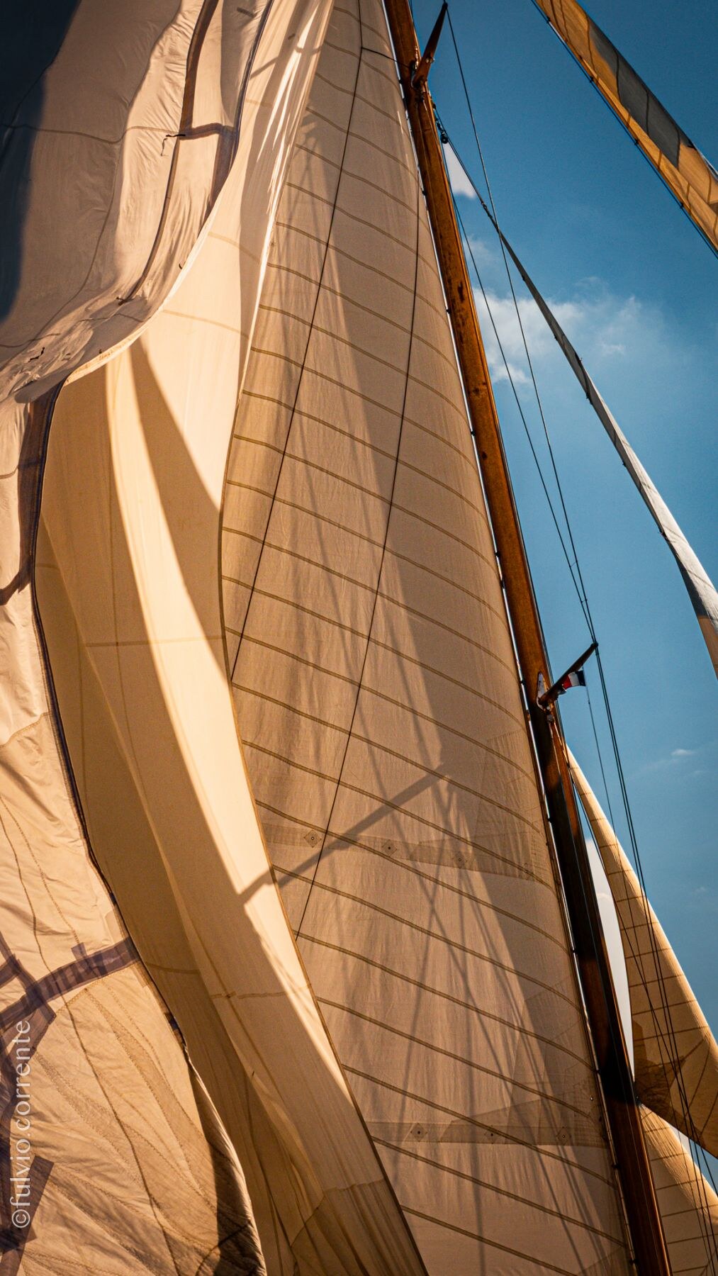 Gros plan sur des voiles ocre en contre-jour et leur mât en bois.