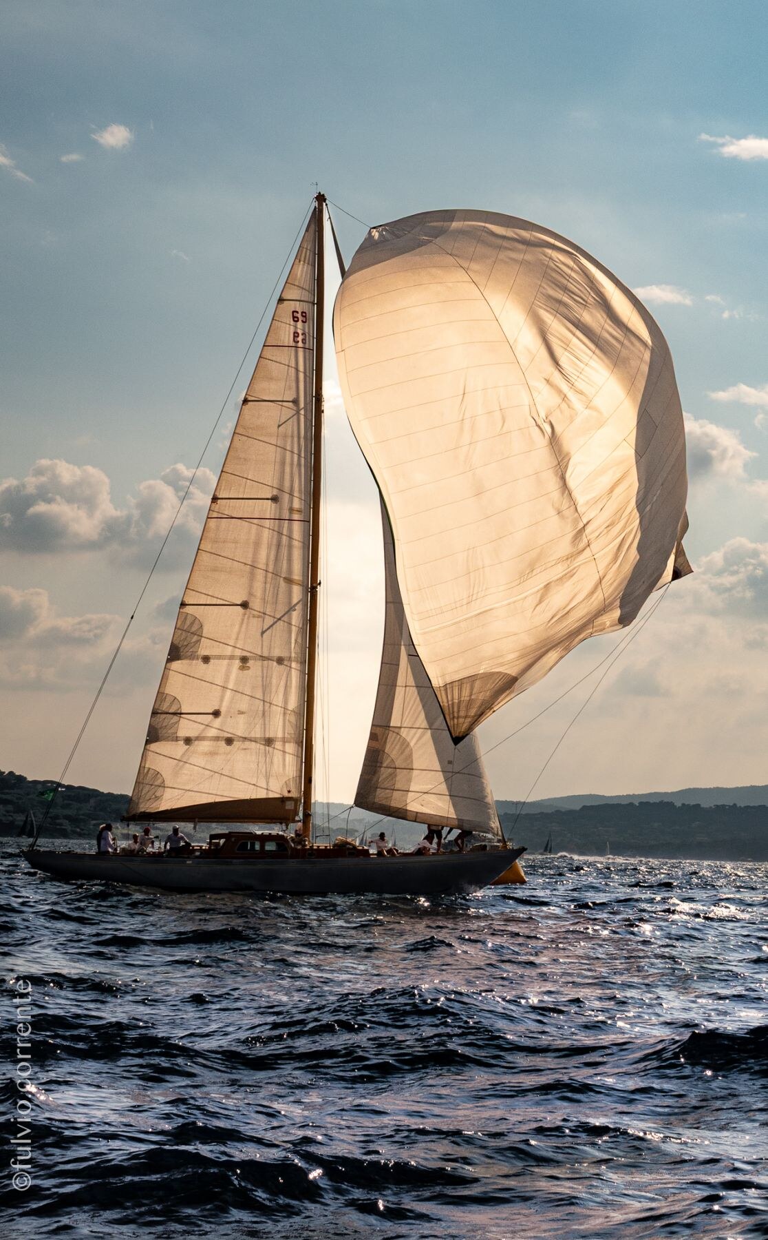 Voilier classique sous un grand spinnaker gonflé, sur une mer sombre et un ciel nuageux.