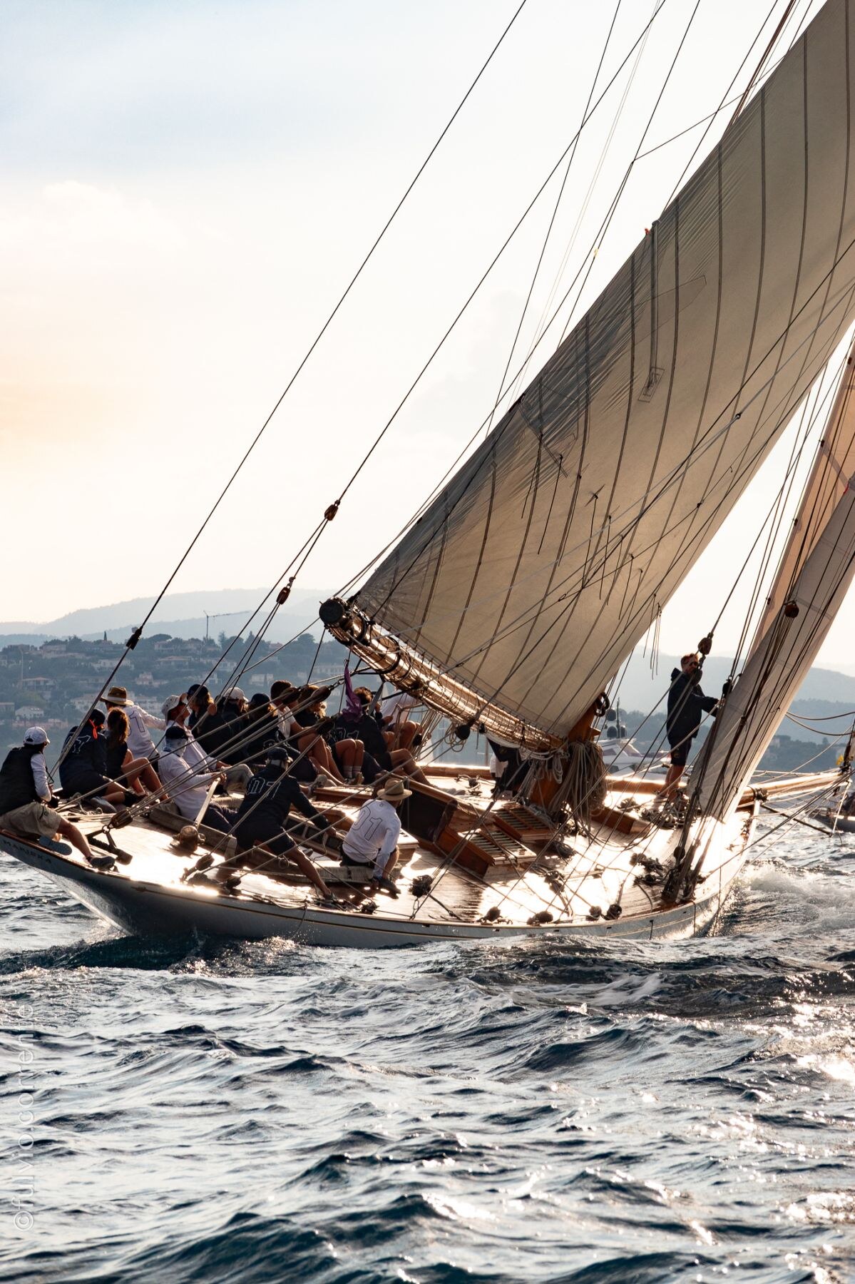 Équipage nombreux à bord d’un voilier gîté, grande voile beige en contre-jour.