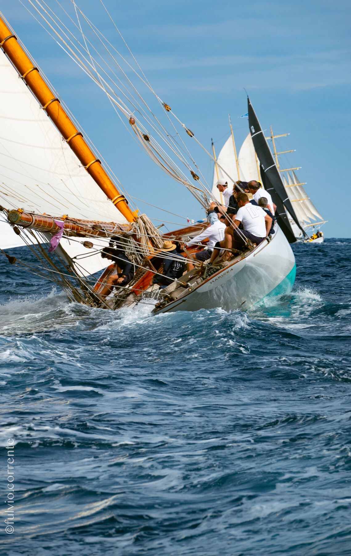 Voilier classique fortement gîté sur une mer agitée, équipage assis au vent.