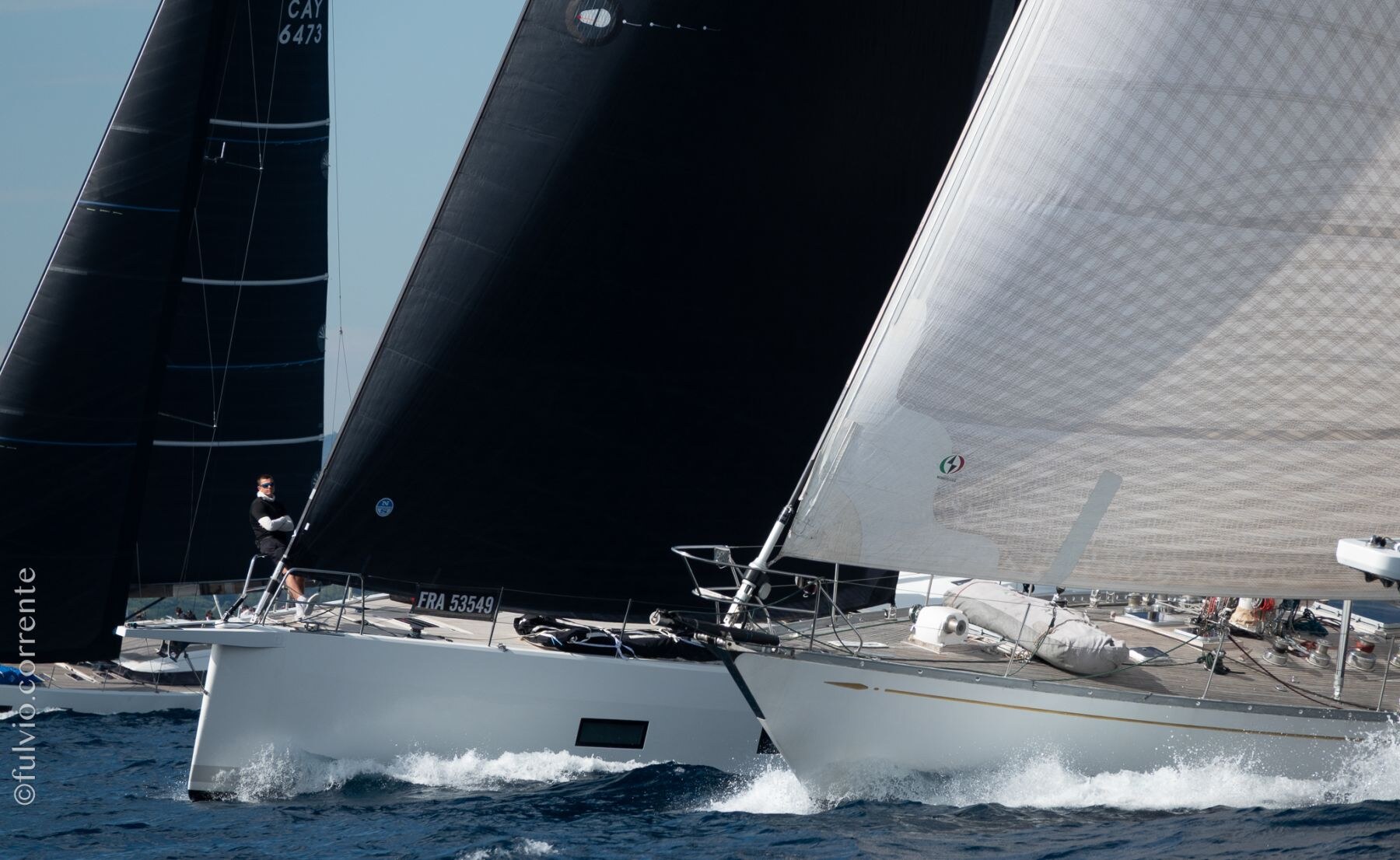 Deux grands voiliers modernes aux voiles noires et grises glissant sur l’eau.