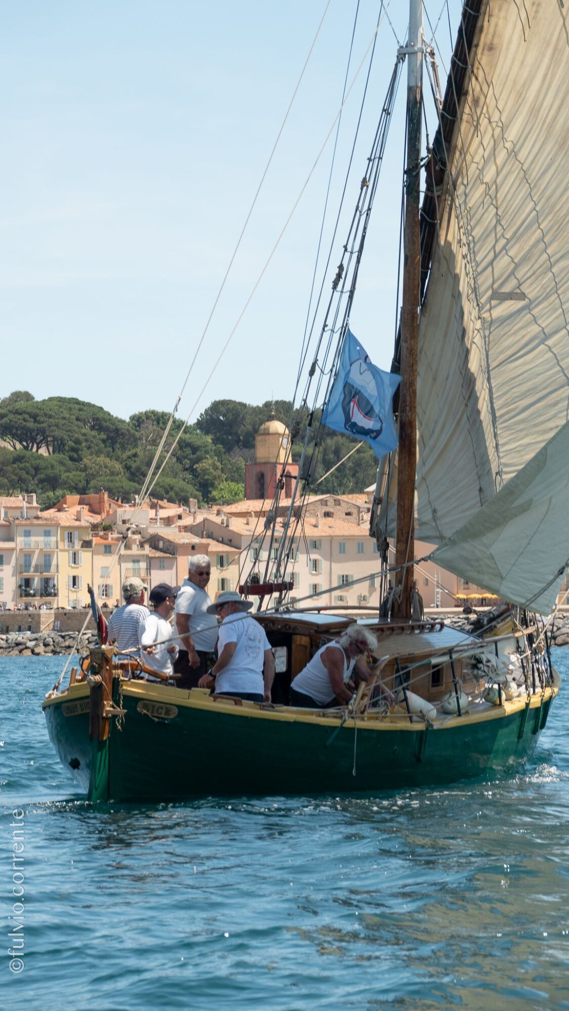 Barque latine à coque verte devant le clocher et les maisons de Saint-Tropez.