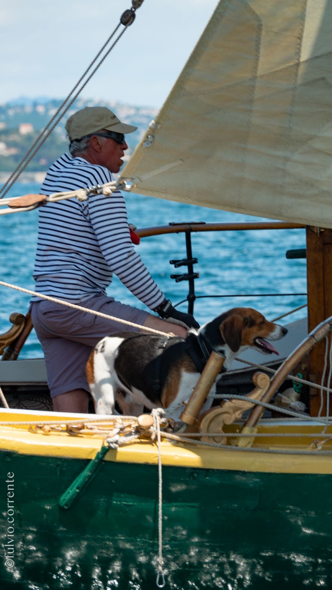 Homme en marinière et son chien beagle à bord d’une barque à coque verte et jaune.