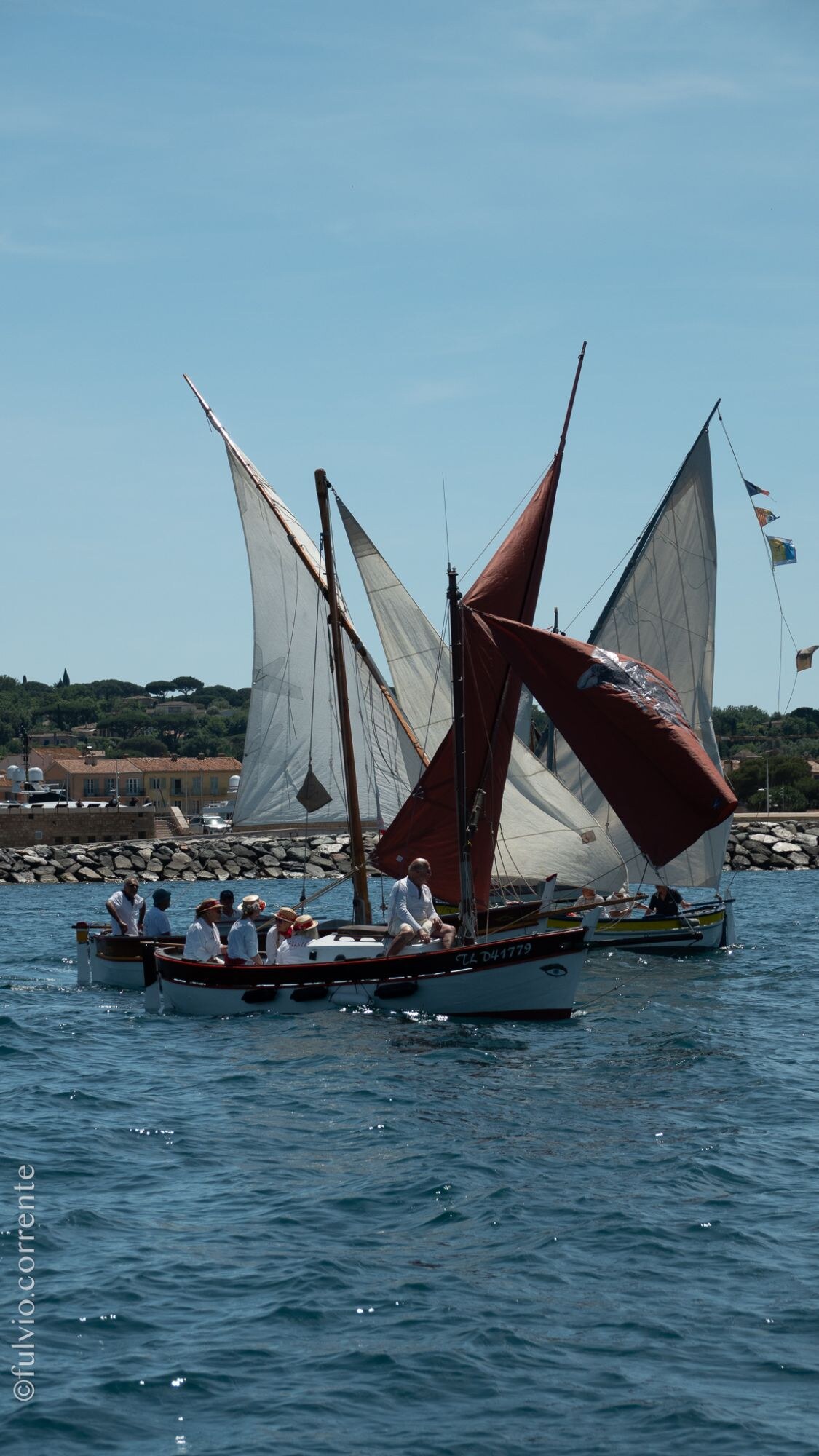 Voiles latines rousses et blanches de plusieurs barques près de la jetée.