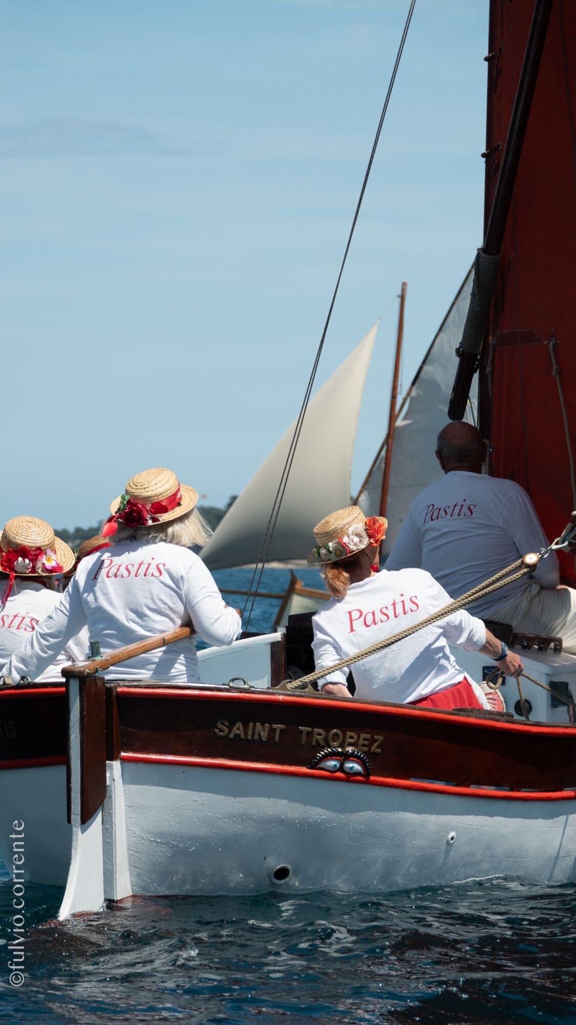Équipiers en t-shirts blancs à l’arrière d’une barque rouge et blanche portant l’inscription Saint-Tropez.