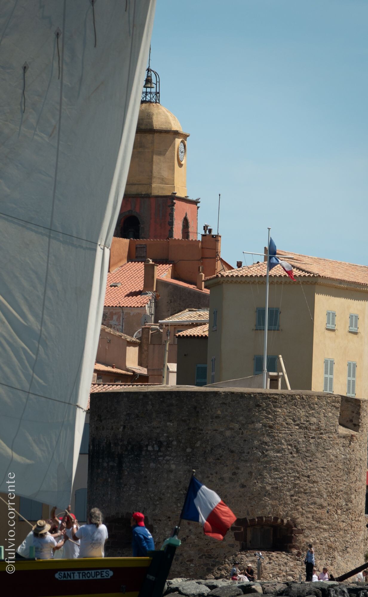 Clocher et tour de Saint-Tropez derrière une grande voile blanche, drapeau tricolore.