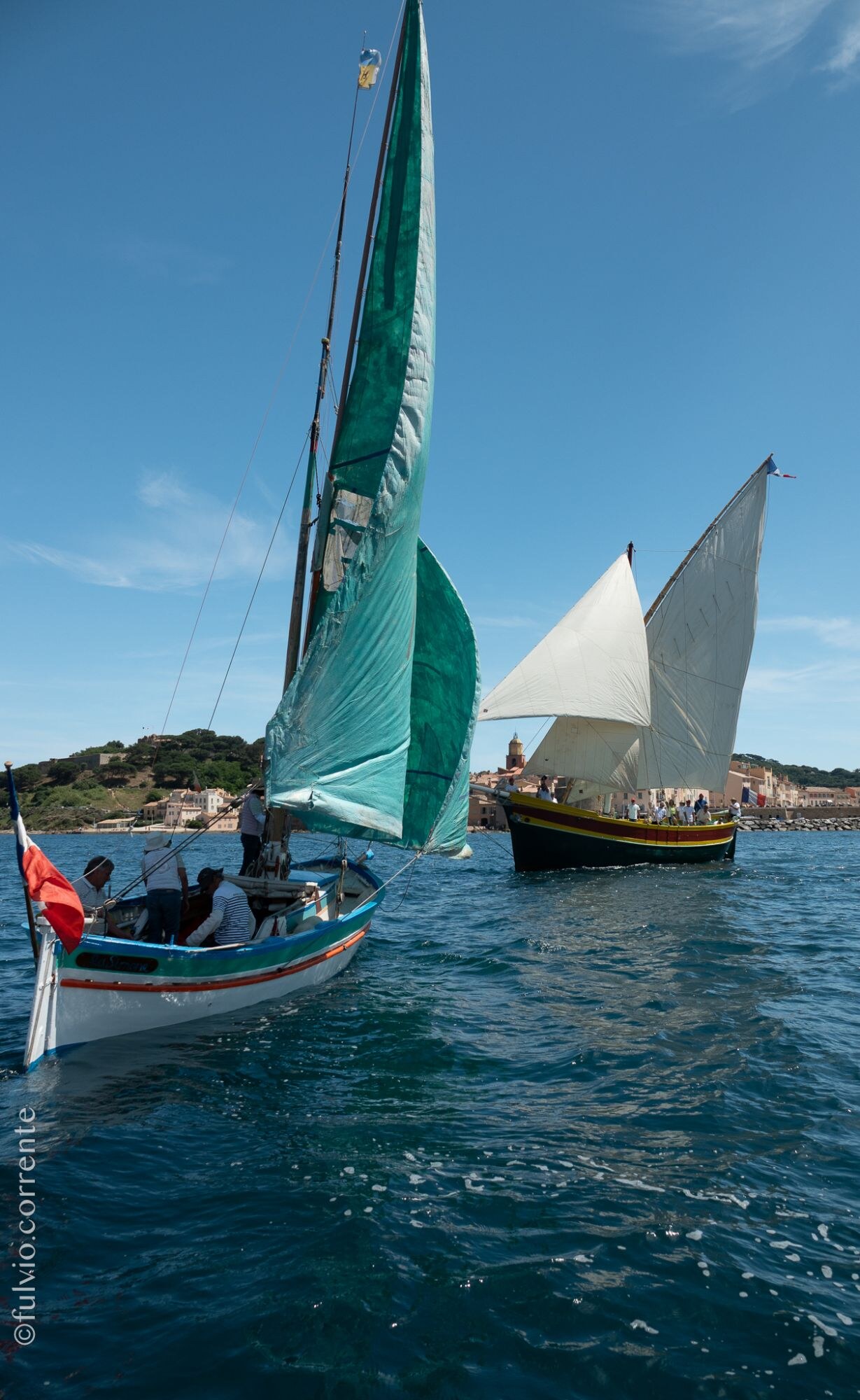 Voiles latines vertes et blanche, barques au large près de la côte.