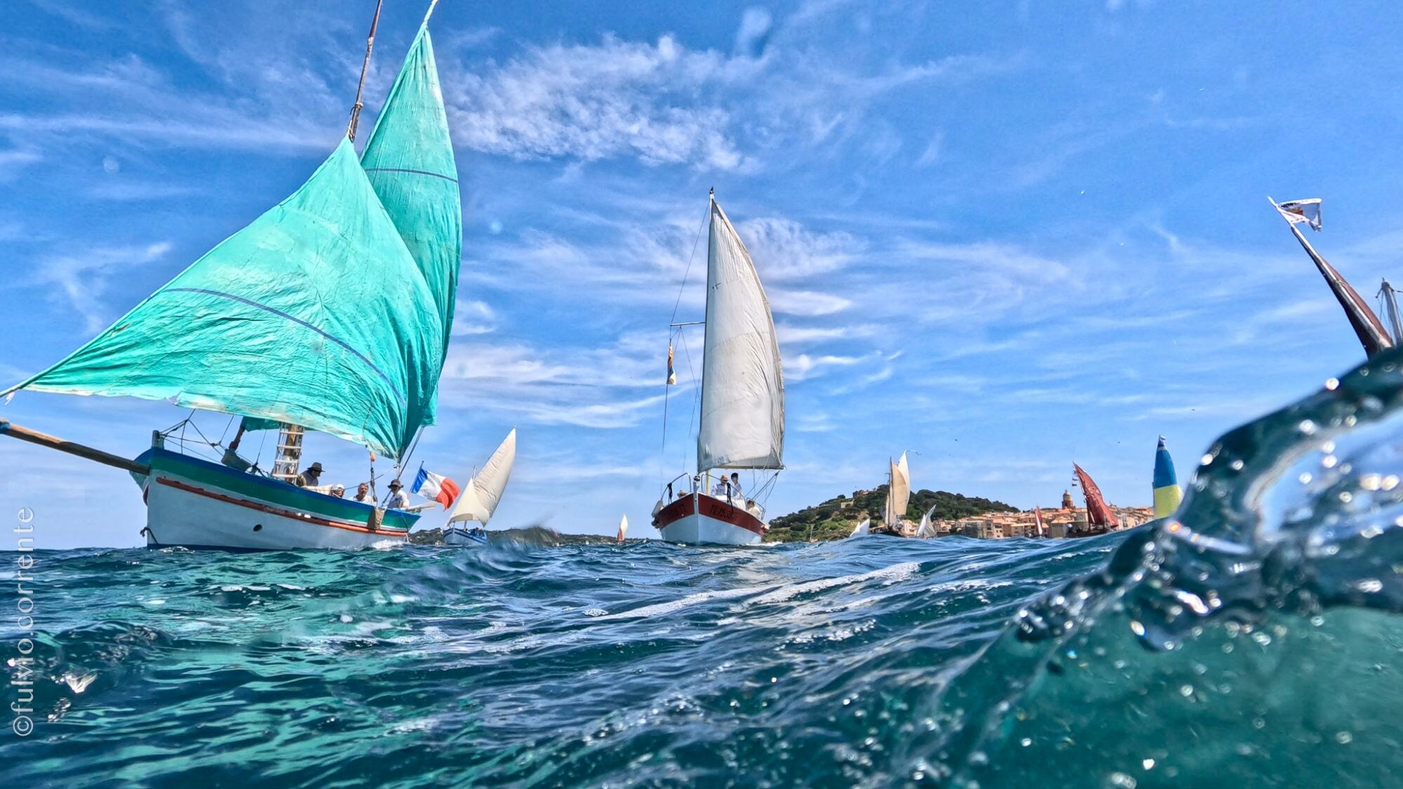 Grande voile vert d’eau gonflée d’une barque, vue au ras des vagues.
