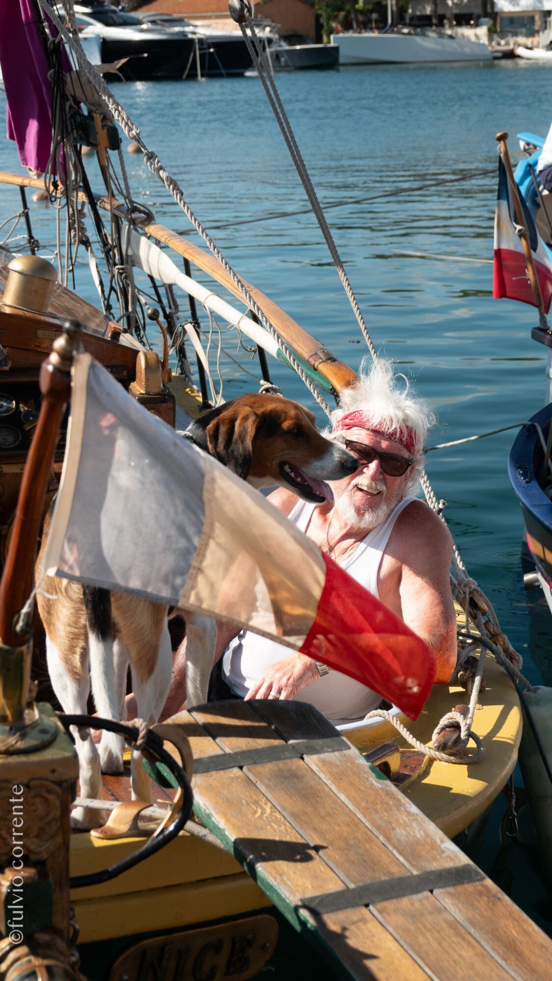 Homme à bandeau rouge et chien beagle à bord d’une barque, drapeau rouge et blanc.