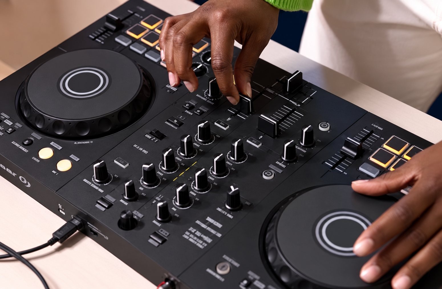 Mains d’un DJ utilisant un contrôleur noir et ses platines.