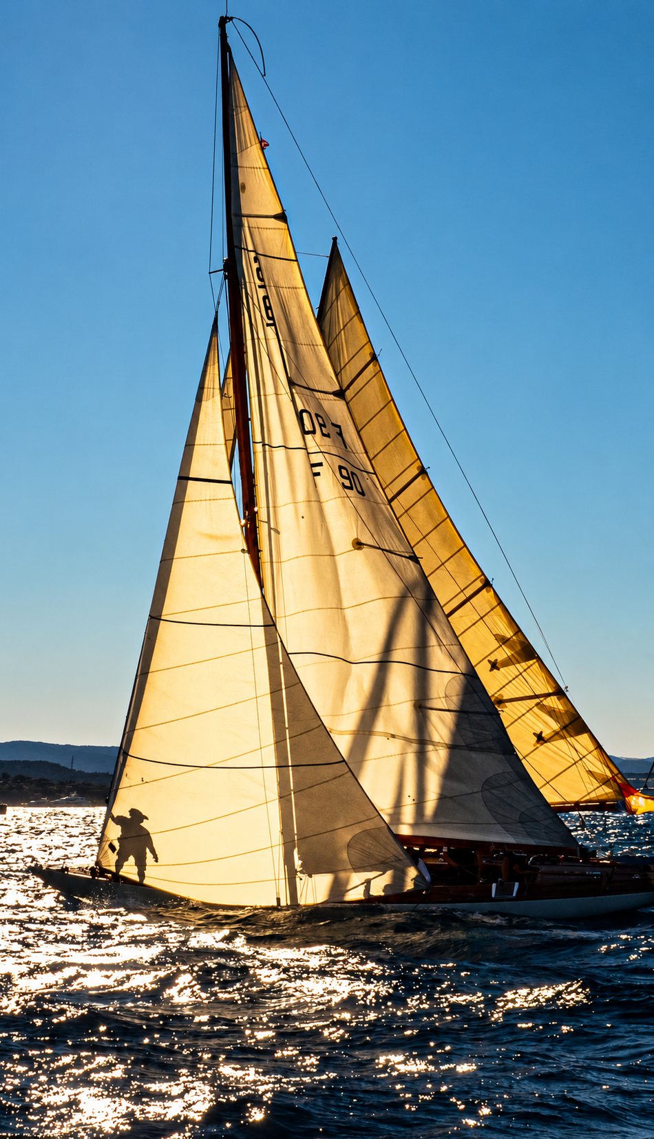 Voilier classique en contre-jour sur une mer scintillante, au coucher du soleil.