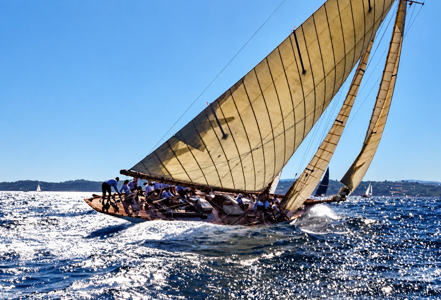 Voilier classique en pleine course, équipage penché sur la mer scintillante.