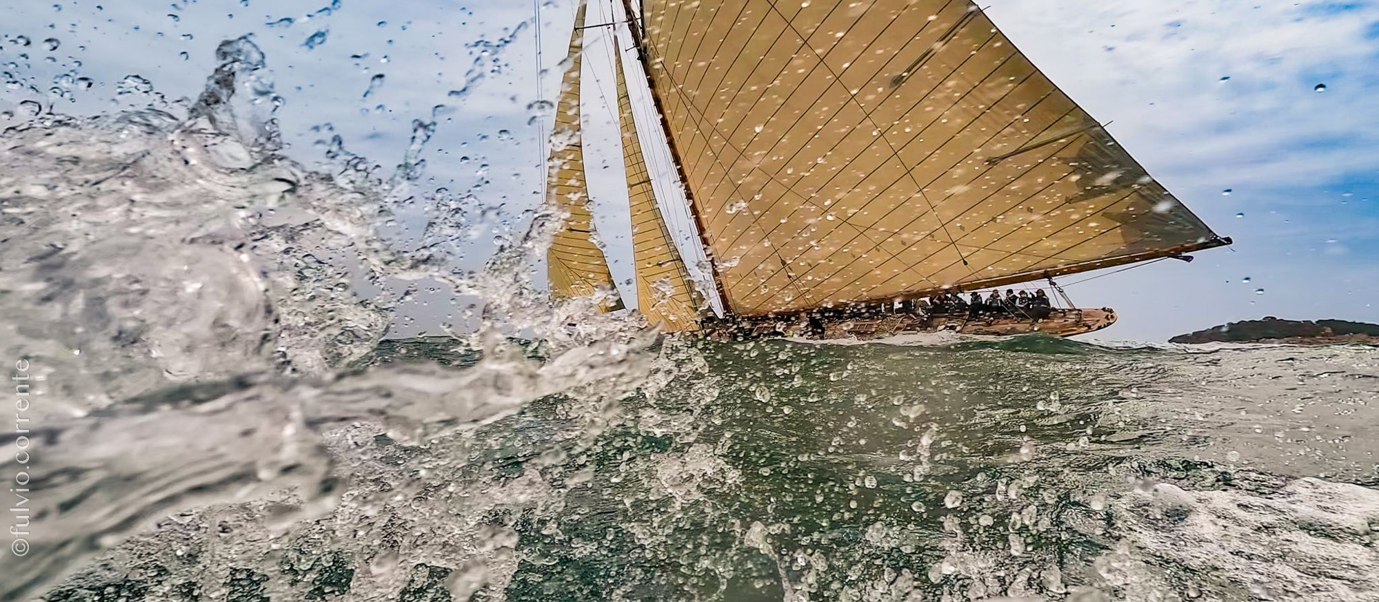 Voilier classique aux voiles dorées fendant les vagues dans les éclaboussures.